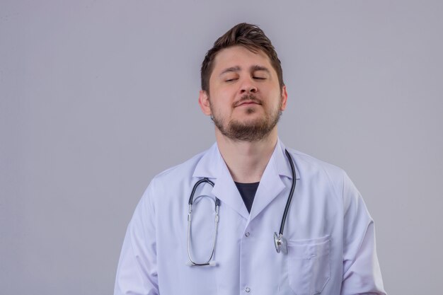 Jeune homme médecin portant blouse blanche et stéthoscope avec expression arrogante regardant vers le bas