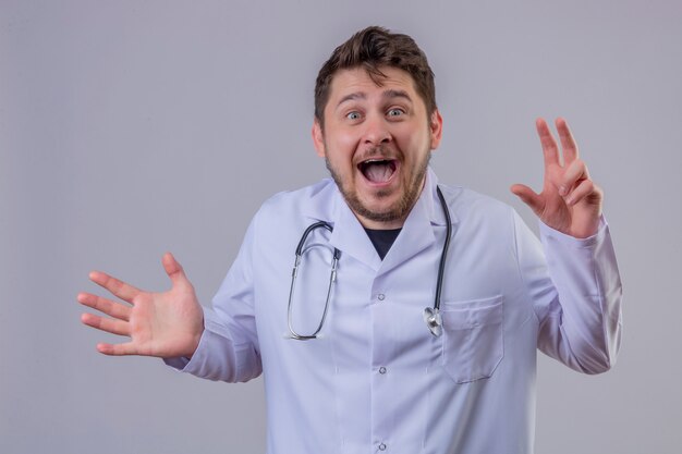 Jeune homme médecin portant blouse blanche et stéthoscope à très surpris et heureux