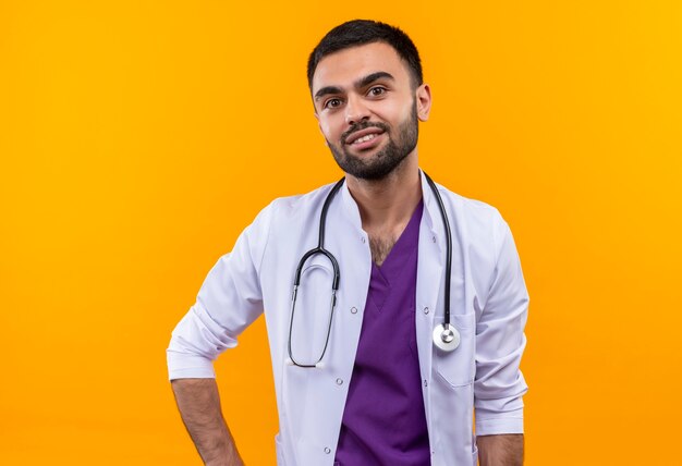 Jeune homme médecin portant une robe médicale stéthoscope sur mur jaune isolé