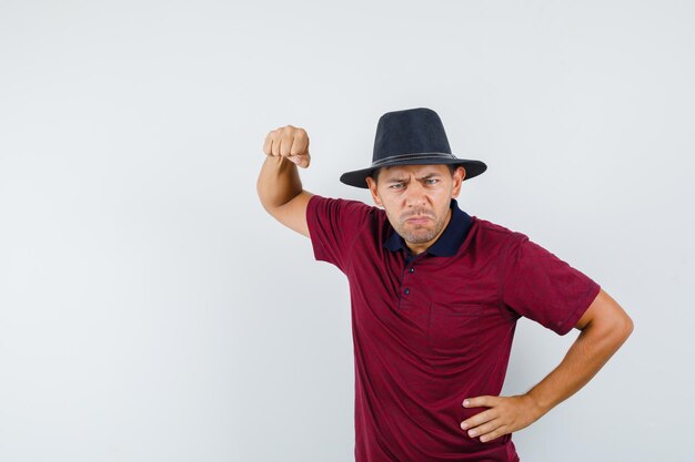 Jeune Homme Menaçant De Poing En T-shirt, Chapeau Et Semblant Nerveux. Vue De Face.