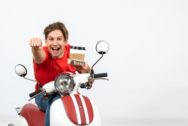 Jeune homme de messagerie heureux en uniforme rouge assis sur un scooter tenant des commandes sur le mur jaune