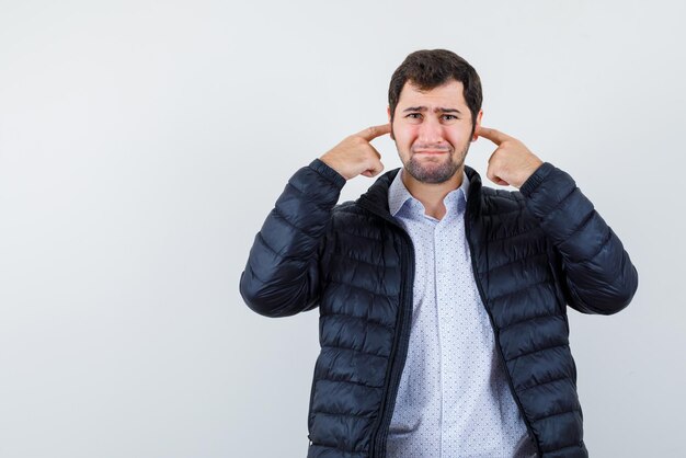 Le jeune homme met ses index dans les oreilles sur fond blanc