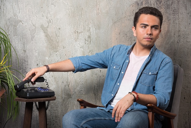 Jeune homme mettant le combiné et assis sur une chaise. Photo de haute qualité