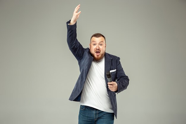 Jeune homme avec microphone sur gris, menant avec microphone au concept de studio.