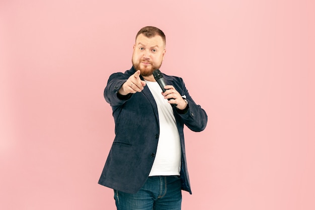 Jeune homme avec microphone sur rose, menant avec microphone au concept de studio.