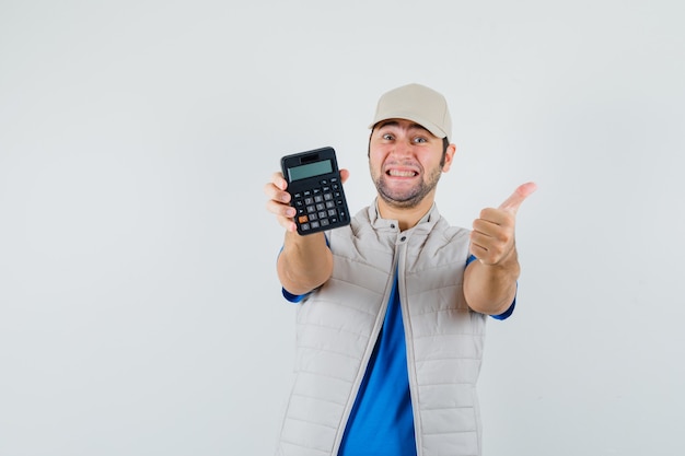 Jeune homme montrant la calculatrice avec le pouce vers le haut en t-shirt, veste et regardant gai, vue de face.