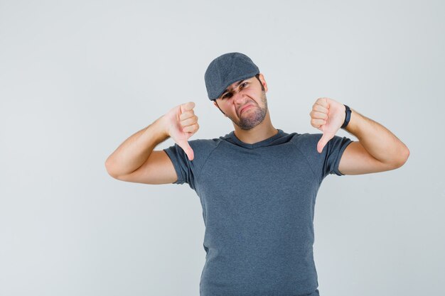 Jeune Homme Montrant Deux Pouces Vers Le Bas En Casquette T-shirt Gris Et à La Déception