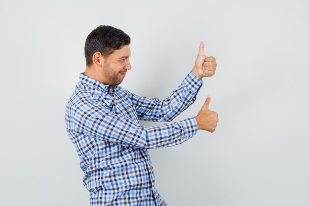 Jeune homme montrant deux pouces vers le haut en chemise à carreaux et à la satisfaction.