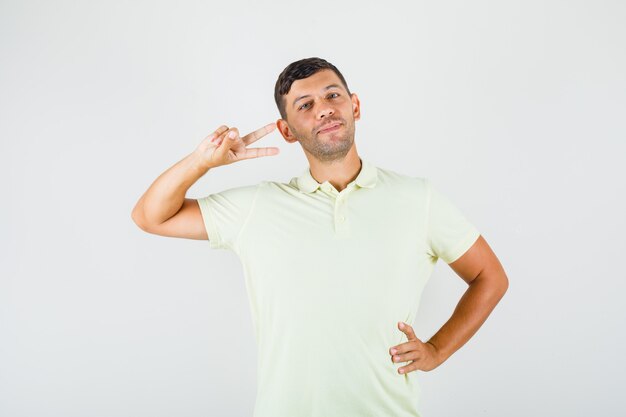 Jeune homme montrant double v-sign avec la main sur la taille en t-shirt et à la confiance
