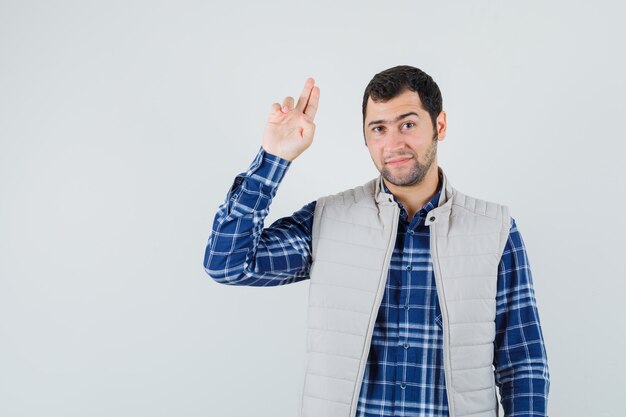 Jeune homme montrant le geste d'adieu en chemise, veste sans manches et à la vue de face, heureux.