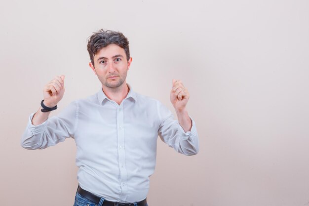 Jeune homme montrant un geste d'argent en chemise blanche et jeans