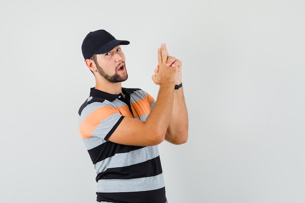 Jeune homme montrant le geste des armes à feu en t-shirt, casquette et à la confiance