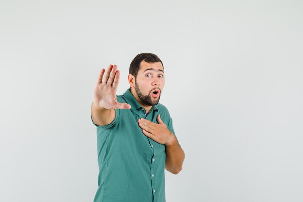 Jeune homme montrant un geste d'arrêt en chemise verte et l'air excité, vue de face.