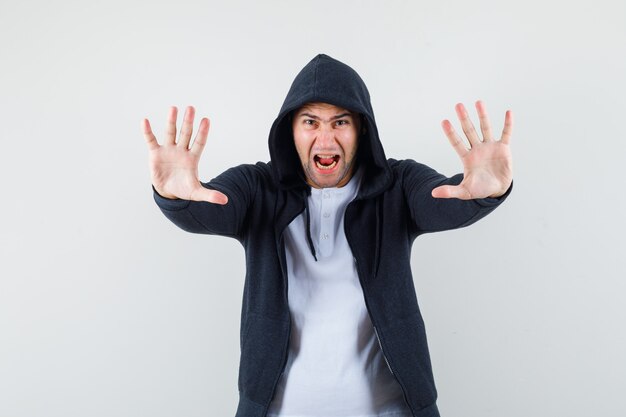 Jeune homme montrant le geste d'arrêt en criant en t-shirt, veste et à l'agitation. vue de face.