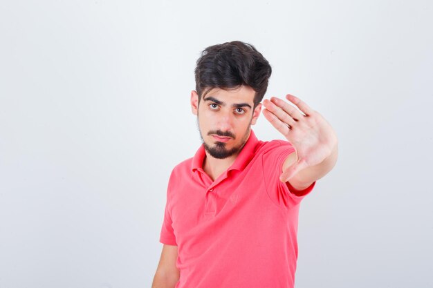 Jeune homme montrant un geste d'arrêt en t-shirt rose et ayant l'air confiant. vue de face.