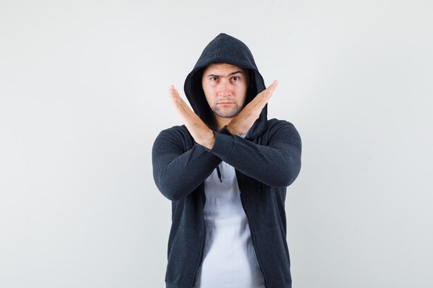 Jeune homme montrant le geste d'arrêt en t-shirt, veste et à la grave, vue de face.