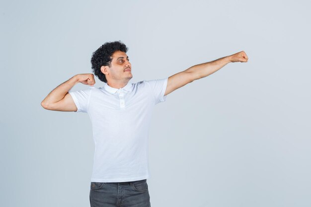 Jeune homme montrant un geste de danse traditionnelle en t-shirt blanc, pantalon et élégant, vue de face.