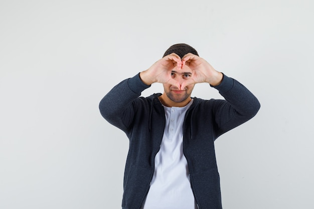 Jeune homme montrant le geste du cœur en t-shirt, veste et à la joyeuse. vue de face.