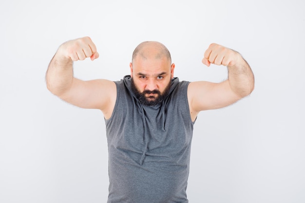 Photo gratuite jeune homme montrant le geste du gagnant en sweat à capuche sans manches et ayant l'air chanceux. vue de face.