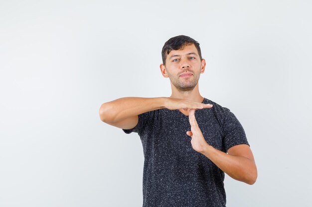 Jeune homme montrant un geste fermé en t-shirt noir et semblant sérieux, vue de face.