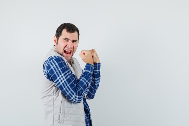 Jeune homme montrant le geste gagnant en chemise, veste et à la joyeuse, vue de face. espace pour le texte