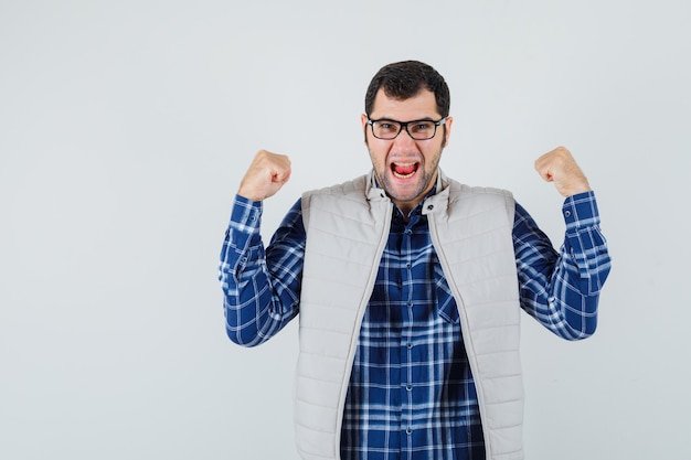 Photo gratuite jeune homme montrant le geste gagnant en chemise, veste, lunettes et à la recherche de bonne humeur. vue de face.