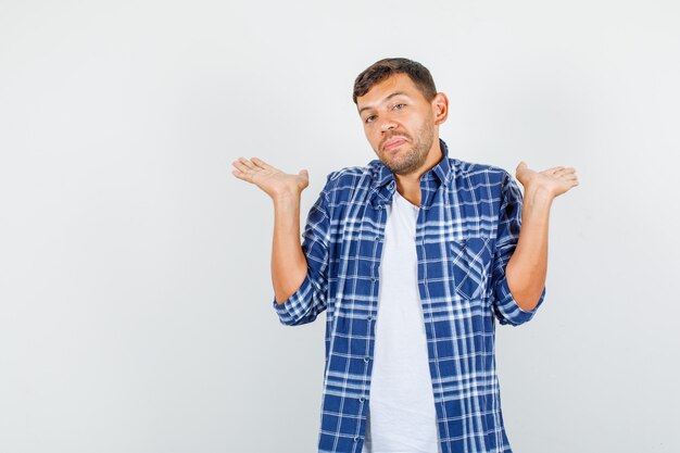 Jeune homme montrant un geste impuissant en chemise et à la perplexité. vue de face.