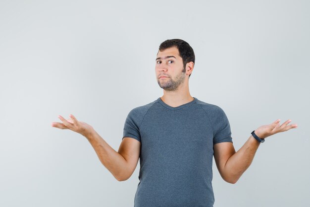 Jeune homme montrant un geste impuissant en t-shirt gris et à la confusion