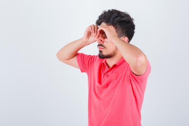 Jeune homme montrant un geste de lunettes en t-shirt et l'air drôle, vue de face.