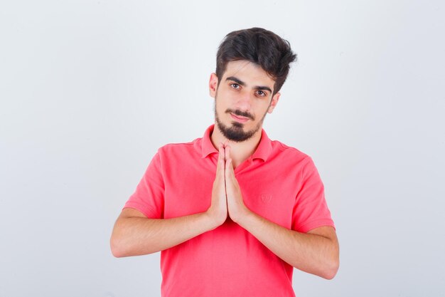 Jeune homme montrant le geste de namaste en t-shirt et semblant paisible, vue de face.