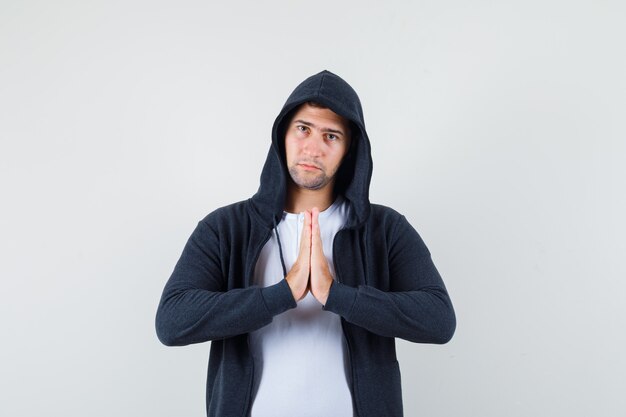 Jeune homme montrant le geste de namaste en t-shirt, veste et à la recherche de calme. vue de face.