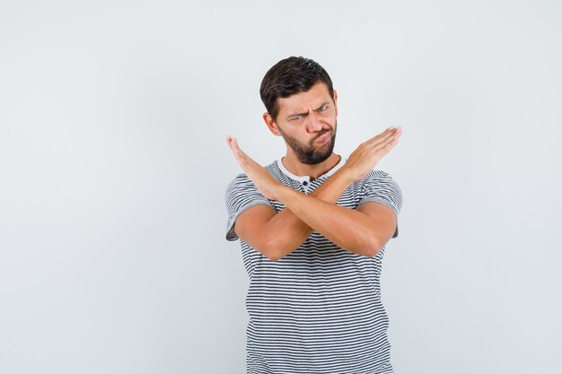 Jeune homme montrant un geste de refus, faisant la grimace en t-shirt et regardant boudeur. vue de face.