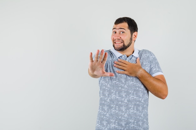 Jeune homme montrant un geste de refus poliment en t-shirt et à la honte. vue de face.