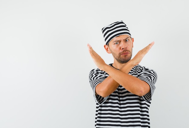 Jeune homme montrant un geste de refus en t-shirt rayé, chapeau et à l'ennui.