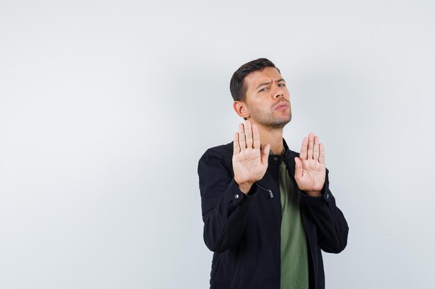 Jeune homme montrant un geste de refus en t-shirt, veste et l'air ennuyé, vue de face.