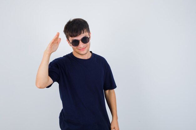 Jeune homme montrant le geste de salut en t-shirt noir et à la vue de face, confiant.