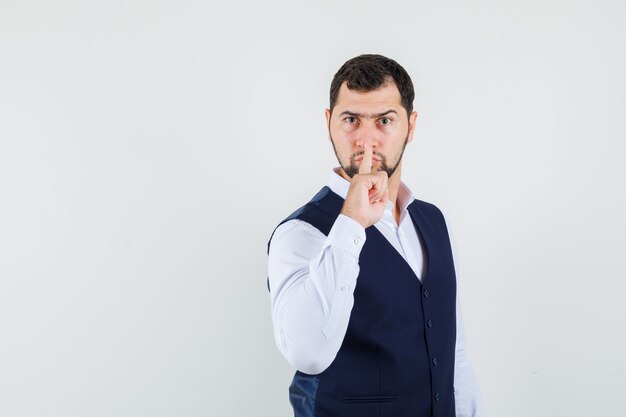 Jeune homme montrant le geste de silence en chemise et gilet et à la sérieuse