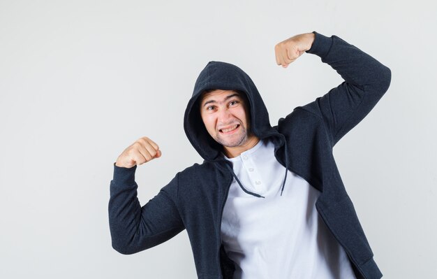 Jeune homme montrant les muscles des bras en t-shirt, veste et à la confiance. vue de face.