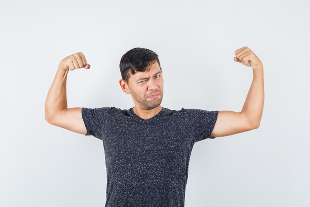 Jeune homme montrant les muscles de ses bras en t-shirt noir et semblant fort, vue de face.