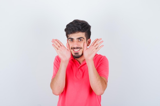 Jeune homme montrant des palmiers en t-shirt rose et ayant l'air confiant. vue de face.