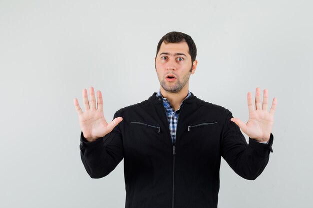 Jeune homme montrant des paumes dans un geste d'abandon en chemise, veste et l'air inquiet. vue de face.