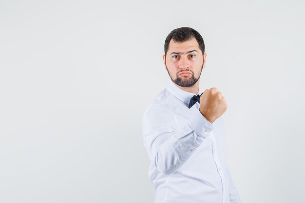 Jeune homme montrant le poing fermé en chemise blanche et à la forte vue de face.