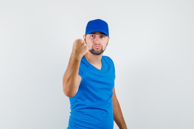 Jeune homme montrant le poing fermé pour menacer en t-shirt bleu et casquette et à furieux