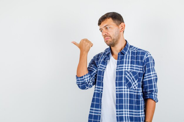 Jeune homme montrant le pouce en chemise et à la confusion. vue de face.