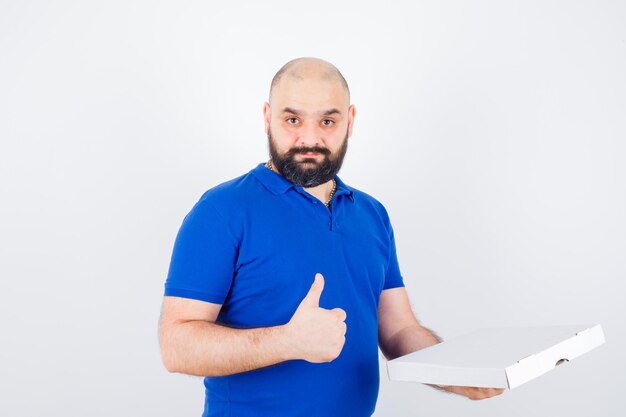 Jeune homme montrant le pouce en t-shirt et ayant l'air confiant. vue de face.