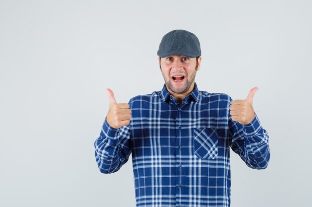 Jeune homme montrant le pouce vers le haut en chemise bleue, casquette et à la recherche de plaisir.