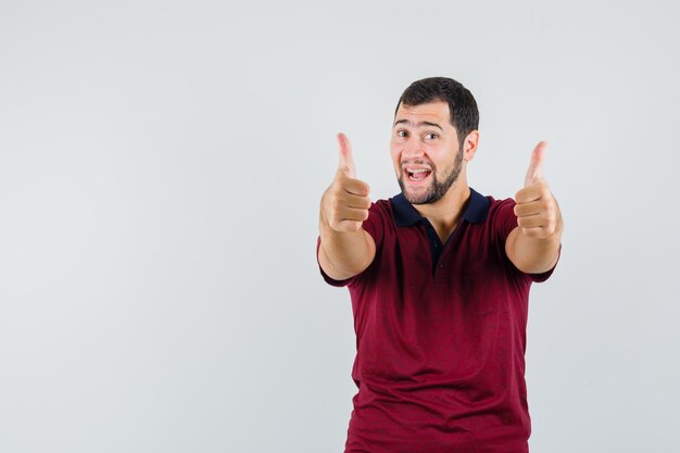 Jeune homme montrant le pouce vers le haut en t-shirt rouge et à la recherche d'énergie. vue de face.