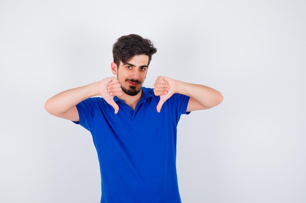 Jeune homme montrant les pouces vers le bas avec les deux mains en t-shirt bleu et à l'optimisme