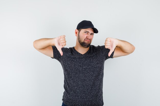 Jeune homme montrant les pouces vers le bas en t-shirt et casquette et à mécontent