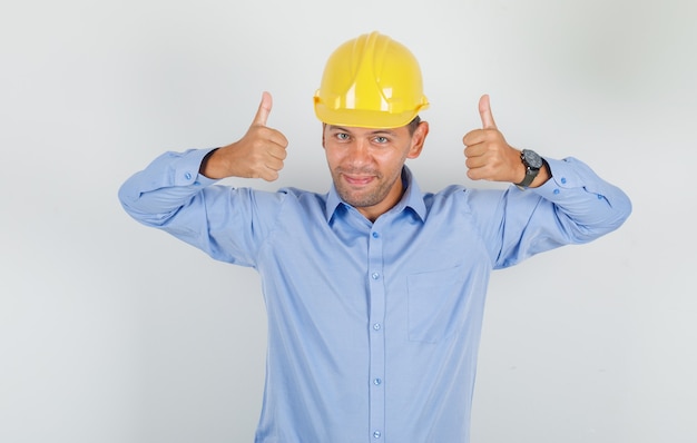 Jeune homme montrant les pouces vers le haut en chemise, casque et air heureux.